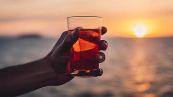 ai généré main en portant verre de cocktail sur floue mer horizon Contexte à coucher de soleil, neural réseau généré image photo