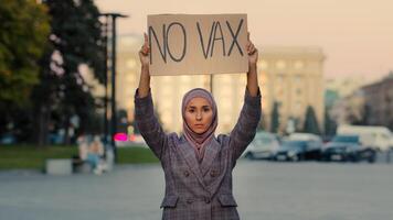 Jeune sérieux musulman femme islamique fille dans hijab femelle activiste des stands dans ville rue protester à l'extérieur en portant signe bannière avec texte non vax contre vaccination refus interdire Arrêtez immunisation manifestation photo