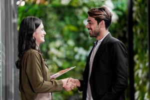 homme d'affaire et décontractée femme d'affaires tremblement mains en plein air. deux Jeune multiculturel collègues de travail traiter pour succès. Contexte de vert mur la nature des arbres. photo