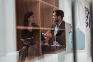 affaires gens parlant à lieu de travail bureau. Masculin et femelle collègues prendre plaisir relaxant et séance sur canapé. collègues discuter à propos le projet dans le bureau. équipe de Jeune gens dans bureau. photo