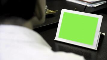 proche en haut pour une femme à la recherche à une blanc tablette avec une vert filtrer. fille dans blanc chemise travail dans Bureau dans de face de tablette avec chrominance clé, arrière voir. photo