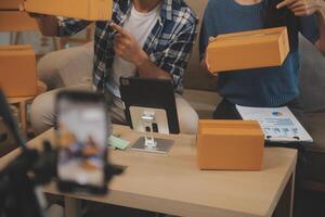 deux asiatique blogueur montrant vêtements dans de face de le caméra à enregistrement vlog vidéo vivre diffusion à sa magasin. en ligne achats Chariot notion. sur canapé à Accueil photo