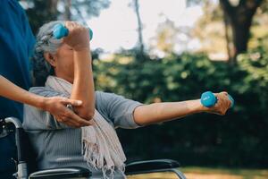 Jeune infirmière ou physiothérapeute dans gommages portion une content retraité vieux femme faire aptitude des exercices avec lumière poids haltères à maison. concept de physiothérapie pour les personnes âgées photo