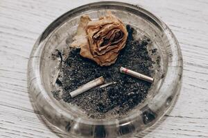 cendrier avec cigarette mégots et une sec rose, le concept de séparation et tristesse. photo