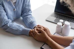 médecin donnant espoir. proche en haut coup de Jeune femelle médecin penché vers l'avant à souriant personnes âgées Dame patient en portant sa main dans palmiers. femme le concierge dans blanc manteau justificatif encourageant vieux la personne photo