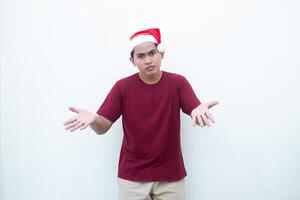 Jeune asiatique homme portant une Père Noël claus chapeau souriant, choc et montrer du doigt à sa côté isolé par blanc Contexte pour visuel la communication photo