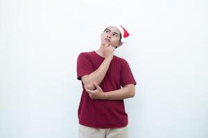 Jeune asiatique homme portant une Père Noël claus chapeau souriant, choc et montrer du doigt à sa côté isolé par blanc Contexte pour visuel la communication photo