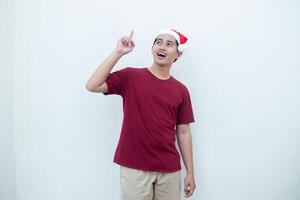 Jeune asiatique homme portant une Père Noël claus chapeau exprimer confusion, pensée, et puis ayant un idée, isolé par une blanc Contexte pour visuel la communication photo