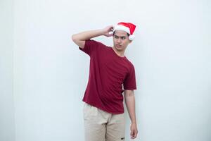 Jeune asiatique homme portant une Père Noël claus chapeau exprimer confusion, pensée, et puis ayant un idée, isolé par une blanc Contexte pour visuel la communication photo