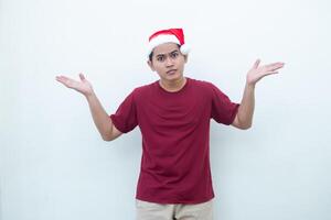 Jeune asiatique homme portant une Père Noël claus chapeau souriant, choc et montrer du doigt à sa côté isolé par blanc Contexte pour visuel la communication photo