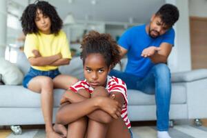 vilain enfant. agacé Parents réprimande leur peu fille pour sa comportement tandis que séance ensemble sur canapé à Accueil photo