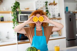 photo de mignonne caucasien femme souriant et en portant deux Orange les pièces tandis que cuisine légume salade dans cuisine intérieur à Accueil