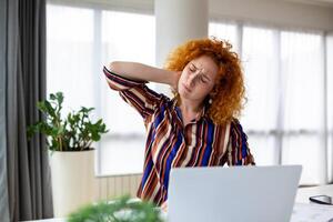 se sentir épuisé. jeune femme frustrée qui a l'air épuisée et se masse le cou alors qu'elle est assise sur son lieu de travail photo