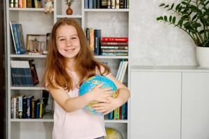 mignonne joyeux fille en portant une globe dans sa mains sur le Contexte de une étagère à livres photo