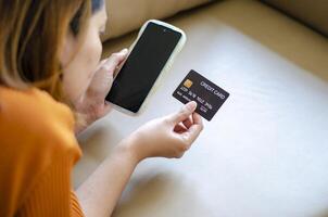 asiatique femme en portant noir crédit carte mensonge sur canapé photo
