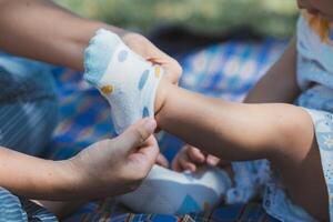 proche en haut de soins asiatique mère en mettant minuscule chaussettes sur de bébé pieds. enfant séance sur herbe. photo