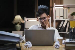 asiatique Jeune fatigué Personnel homme d'affaire en utilisant bureau ordinateur ayant surmenage projet pendant la nuit dans bureau. photo