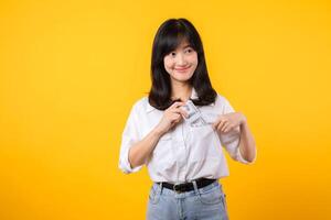 captivant image de asiatique Jeune femme portant blanc chemise et denim jeans, en toute confiance en portant en espèces de sa chemise poche. mode se rencontre financier autonomisation. parfait pour la finance et mode thèmes. photo