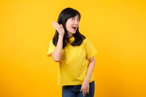 Capturer attention portrait de Jeune asiatique femme. portant une Jaune T-shirt et denim jeans, penche dans à surprendre et écouter, évoquant curiosité et intrigue. accrocheur promotions et remises. photo