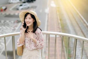 Jeune asiatique femme voyageur avec tissage panier en utilisant mobile téléphone et permanent sur dépasser avec chemin de fer Contexte. périple voyage mode de vie, monde Voyage explorateur ou Asie été tourisme concept. photo