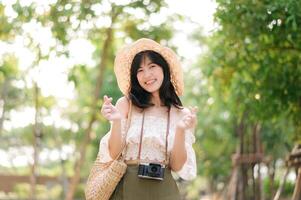 portrait de asiatique Jeune femme voyageur avec tissage chapeau et panier et une caméra sur vert Publique parc la nature Contexte. périple voyage mode de vie, monde Voyage explorateur ou Asie été tourisme concept. photo