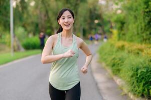 en forme asiatique Jeune femme le jogging dans parc souriant content fonctionnement et profiter une en bonne santé Extérieur mode de vie. femelle joggeur. aptitude coureur fille dans Publique parc. en bonne santé mode de vie et bien-être étant concept photo