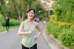 en forme asiatique Jeune femme le jogging dans parc souriant content fonctionnement et profiter une en bonne santé Extérieur mode de vie. femelle joggeur. aptitude coureur fille dans Publique parc. en bonne santé mode de vie et bien-être étant concept photo