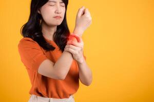 mise en évidence arthrite soins de santé, 30s asiatique femme portant Orange chemise tandis que en portant sa poignet dans douleur. illustrant le défis de poignet arthrite, sert comme concept pour soins de santé et bien-être. photo