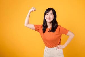 ressentir habilité avec une Jeune asiatique femme dans sa 30s célébrer une poing en haut main signe geste, portant un Orange chemise sur Jaune Contexte. responsabilisation et féminisme concept. photo