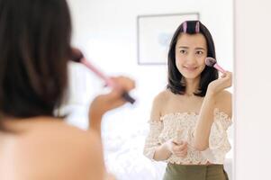 magnifique Jeune asiatique femme appliquant maquillage dans de face de le miroir. mode de vie gens concept. publicité pour peau crème, anti-rides crème, bébé visage photo