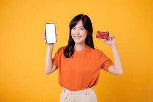 de bonne humeur asiatique femme dans sa 30s, révélateur téléphone intelligent et crédit carte sur Jaune Contexte. lisse en ligne Paiement achats. photo