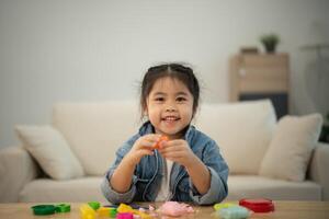 asiatique mignonne peu fille apprentissage et en jouant à utilisation coloré jouer pâte dans le vivant pièce à le maison. bébé activité éducation développement mode de vie concept. photo