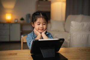 asiatique enfant fille à la recherche en utilisant et toucher tablette afficher filtrer. bébé souriant marrant temps à utilisation tablette. aussi beaucoup écran temps. mignonne fille en train de regarder vidéos tandis que la télé, l'Internet dépendance concept. photo
