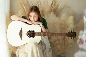 portrait de adolescent fille avec longue cheveux dans vert robe en jouant acoustique guitare. photo