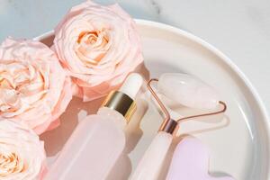 huile essentielle de rose cosmétique et rouleau de quartz rose masseur facial pierre gua-sha pour un massage de beauté du visage à la maison. concept de soins de la peau et de traitement du visage. photo