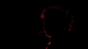 homme avec une cigarette dans le sien bouche vu dans profil dans silhouette avec rouge lumière éclairant le sien profil contre noir Contexte photo