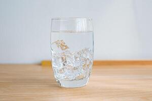 un clair verre avec la glace et eau, en bois sol et blanc Contexte. photo