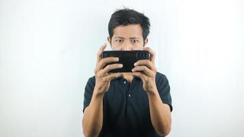 asiatique homme avec une sérieux expression est en jouant une Jeu sur le sien cellule téléphone. photo