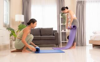 yoga à maison. en bonne santé aptitude classe deux femme roulant exercice tapis dans vivant pièce après classe avec bonheur photo