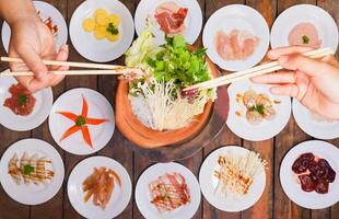 Haut table nourriture main de gens en utilisant baguettes pinces de Frais porc et brut porc foie ventre. préparer à aller vers le bas à shabu chaud pot. délicieux asiatique grillé cuisine photo