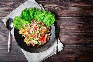 Papaye salade avec calamar tentacules, séché crevette, tomates, longue des haricots et cacahuètes chevronné avec poisson sauce, sucre, et citron vert sur une assiette mis sur une en bois conseil, en quittant espace pour des lettres. photo