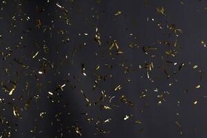 de fête fête ou carnaval décoration d'or brillant confettis et enroulé banderoles chute contre noir Contexte. photo