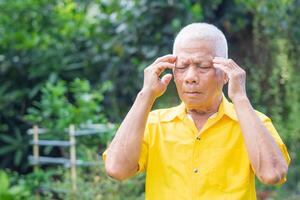 Sénior homme avec une mal de tête, sentiment douleur, et avec un expression de étant indisposé tandis que permanent dans le jardin. cerveau maladies problème cause chronique sévère maux de tête photo