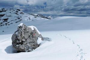 randonnée Piste marqueur dans le montagnes pendant l'hiver. trace de pas la gauche par une alpiniste. neigeux blanc paysage. rouge et blanc marque à suivre le chemin. randonnée et alpinisme concept. photo