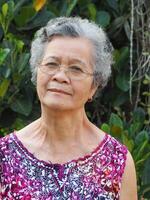 portrait de une Sénior femme souriant et à la recherche à caméra tandis que permanent dans une jardin photo