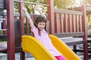 mignonne asiatique fille en jouant sur le faire glisser dans le terrain de jeux photo