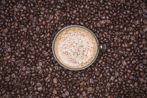 tasse de cappuccino placée dans une assiette de grains de café, avec fond de grains de café torréfiés plein cadre photo