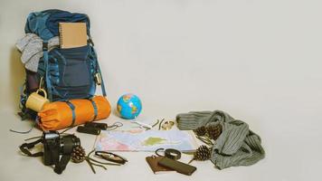 vacances de planification touristique à l'aide de la carte du monde avec d'autres accessoires de voyage autour. smartphone, appareil photo argentique et lunettes de soleil sur fond blanc. sac à dos de voyage