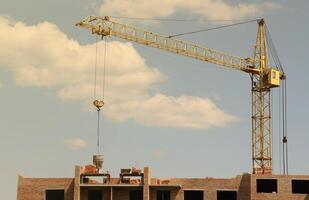 vue de une grand construction site avec bâtiments en dessous de construction et à plusieurs étages Résidentiel maisons. la tour grues dans action sur bleu ciel Contexte. logement rénovation concept photo