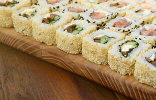 gros plan d'un grand nombre de rouleaux de sushi avec différentes garnitures se trouvent sur une surface en bois. photo macro de plats japonais classiques cuits avec un espace de copie